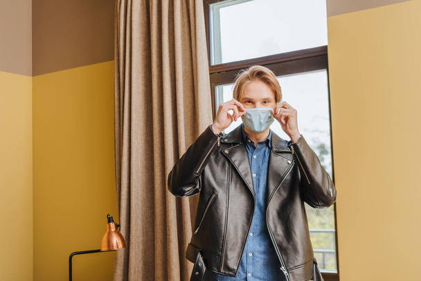 man in jacket touching medical mask at home, end of quarantine concept  - Фото, изображение