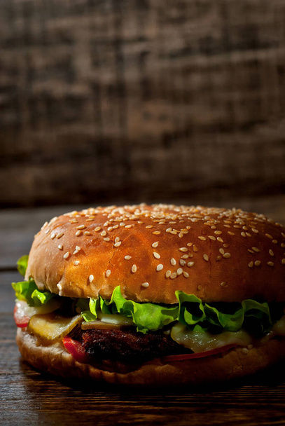 Burger on a dark wooden board. Cheeseburger with cutlet and herbs on black background. Food with contrasting dramatic light. Bun closeup. - Zdjęcie, obraz