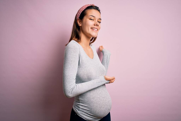 Fiatal gyönyörű tinédzser lány terhes vár baba felett elszigetelt rózsaszín háttér Meghívó belépni mosolygós természetes nyitott kézzel - Fotó, kép