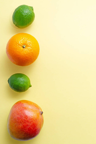 Fresh juicy exotic fruits orange limes mangoes on a yellow uniform background. citrus vitamin c healthy eating and lifestyle minimalism fruit diet slimming close-up with place for text - Fotó, kép