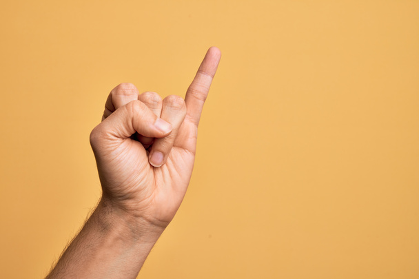 Hand van Kaukasische jongeman met vingers over geïsoleerde gele achtergrond met kleine vinger als pinky belofte inzet, nummer een - Foto, afbeelding