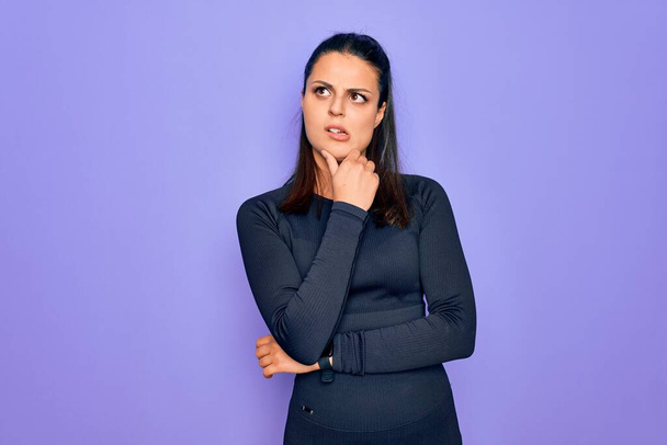 Young beautiful brunette sporty woman wearing casual sportswear over purple background Thinking worried about a question, concerned and nervous with hand on chin - Photo, Image
