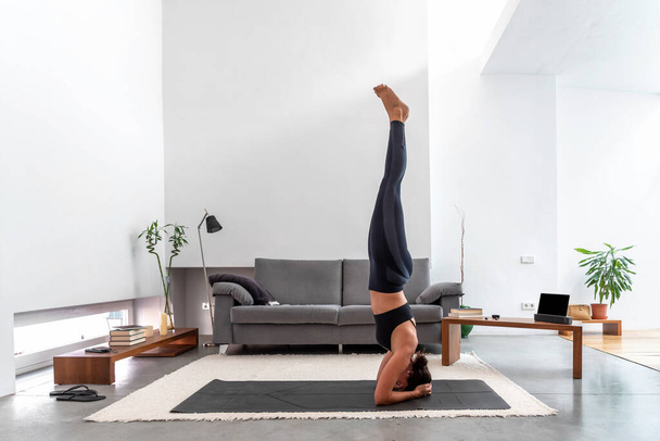Fit woman practicing a headstand exercise, (salamba sirsasana pose) at her cozy home - Photo, Image