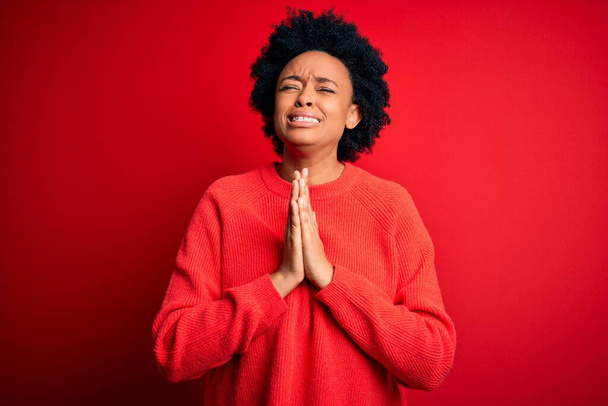 Young beautiful African American afro woman with curly hair wearing casual sweater begging and praying with hands together with hope expression on face very emotional and worried. Begging. - Photo, Image