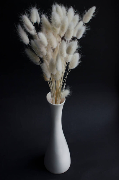 Getrocknete weiße Kräuter in weißer Vase auf schwarzem Hintergrund, Vorderseite - Foto, Bild