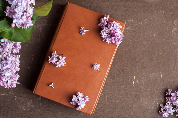 old book and braold book and branches of lilac on a brown background. top view - Fotografie, Obrázek