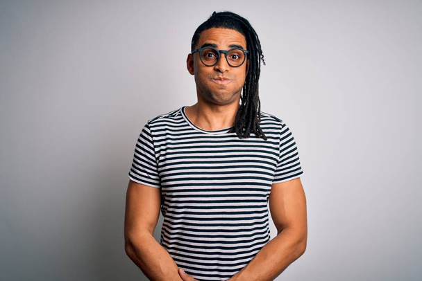 Young handsome african american man with dreadlocks wearing striped t-shirt and glasses puffing cheeks with funny face. Mouth inflated with air, crazy expression. - Foto, imagen