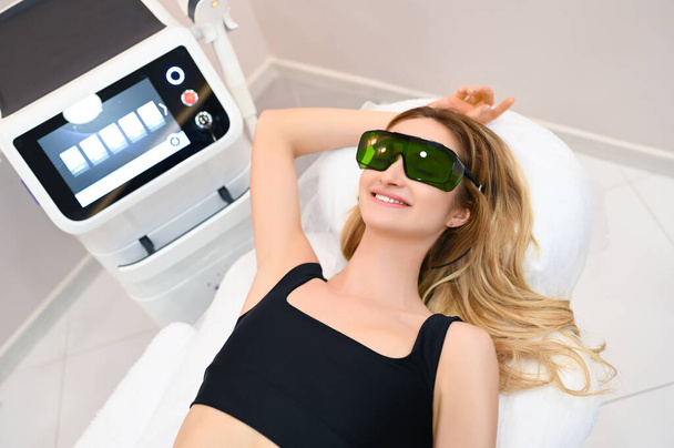 Laser epilation and cosmetology in beauty salon. Hair removal procedure. Laser epilation, cosmetology, spa, and hair removal concept. Beautiful blonde woman getting hair removing on armpits - Photo, Image