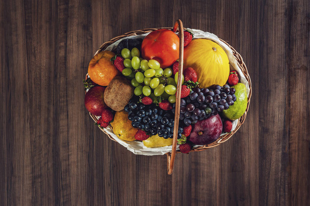 Top view of a basket and fresh fruits on wooden background - Foto, imagen