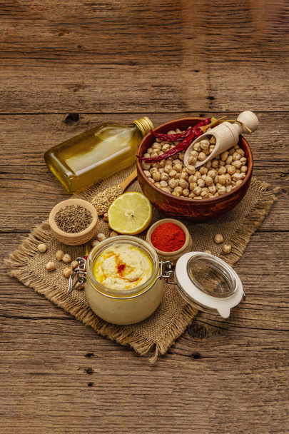 Hummus on old wooden boards background. Dry chickpea, olive oil, lemon, cumin and chili pepper. Traditional food in Middle Eastern and Mediterranean cuisine - Foto, Imagen