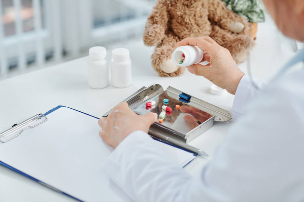 Médico vaciando tabletas y pastillas en una bandeja de metal y escribiendo la receta para el paciente - Foto, imagen