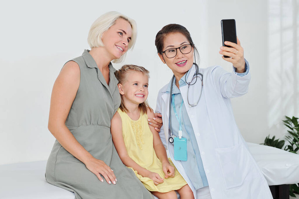 Happy Vietnamese pediatrician taking selfie with her recovered little patient and her mother - 写真・画像