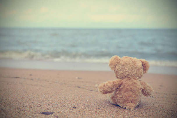 Solo orsacchiotto seduto sulla spiaggia guardare sul mare si sentono soli. Immagine in stile vintage con spazio di copia
. - Foto, immagini