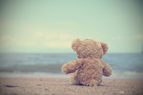 Samotný medvídek sedící na pláži a dívající se na moře se cítí osamělý. Styl vintage obrázku s prostorem pro kopírování. - Fotografie, Obrázek