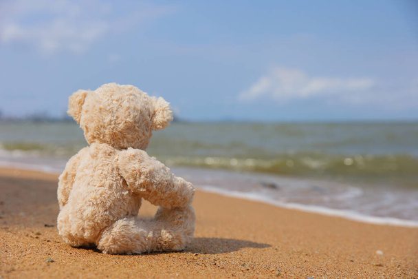 Único urso de pelúcia sentado na praia sozinho olhar no mar
. - Foto, Imagem