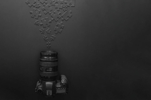 Die Kamera liegt auf schwarzem Hintergrund neben schwarzen Puzzles, die sich auf der Kameralinse ansammeln. Konzept für eine professionelle Fotografen- oder Fotoschule - Foto, Bild