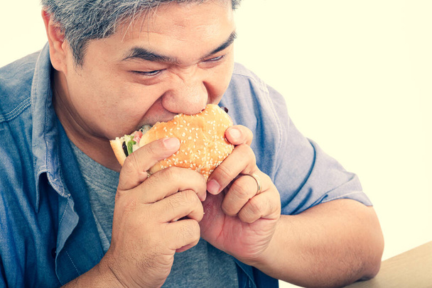 Hamburger yiyen şişman yaşlı bir adam. Yaşlılar için sağlıklı yiyecekler yeme kavramı - Fotoğraf, Görsel