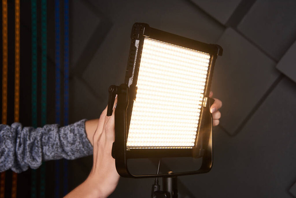 Studioassistent befestigen professionelles Videolicht auf verstellbarem Lichtstativ. LED-Lampe auf Stativ im Fotostudio. Foto- und Videolampe auf geprägtem grauen Wandhintergrund. Nahaufnahme - Foto, Bild
