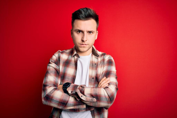 Young handsome caucasian man wearing casual modern shirt over red isolated background skeptic and nervous, disapproving expression on face with crossed arms. Negative person. - Photo, Image