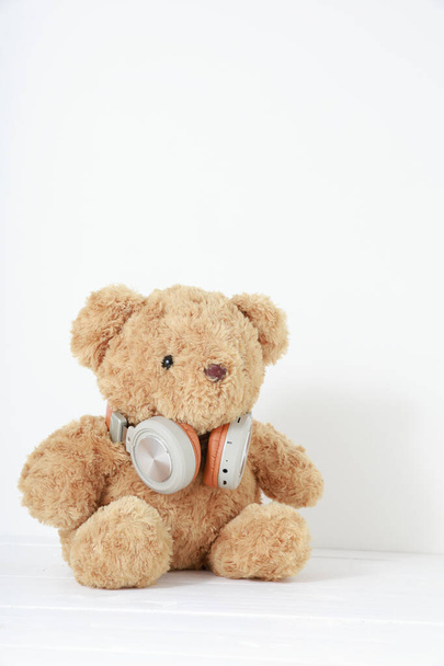Single bruine teddybeer zittend op wit hout met koptelefoon witte achterzijde. - Foto, afbeelding