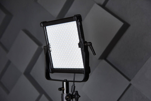 studio assistant fix professional video light on adjustable light stand. Led lamp on tripod in photo studio. Photo and video lamp on embossed grey wall background. Close-up view - Photo, Image