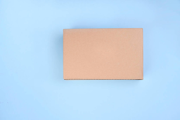Craft unlabeled cardboard package box presented on stressed brushed on a blue background. The concept of delivery, mail, destinations, the quarantine period is relevant. Copy space. Above. - Foto, Imagem
