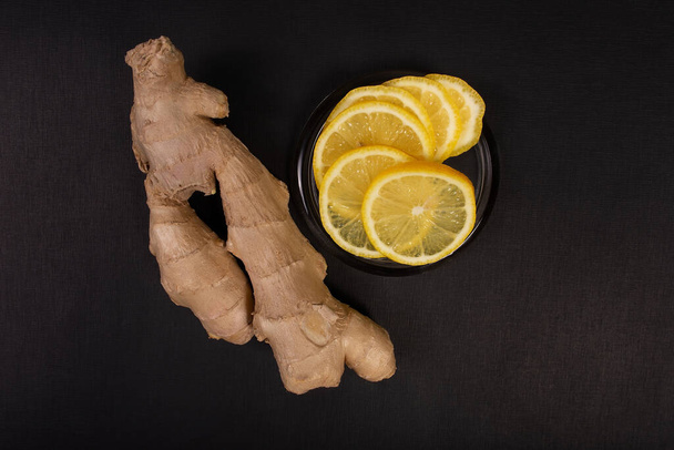 Zitrone und Ingwerwurzel auf schwarzem Hintergrund schneiden - Foto, Bild