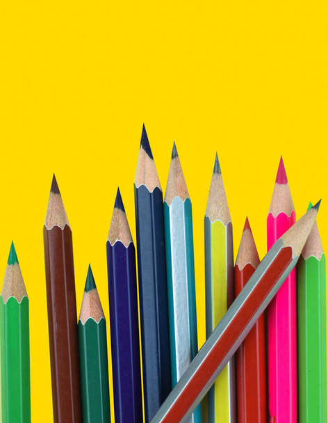 Fila de diferentes lápices de colores colocados sobre un fondo de papel amarillo
 - Foto, imagen