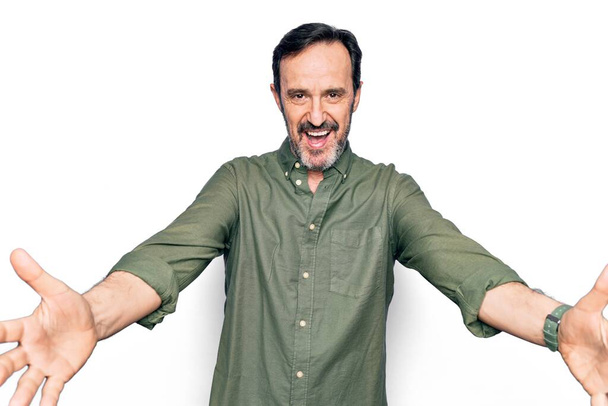 Middle age handsome man wearing casual green shirt over isolated white background looking at the camera smiling with open arms for hug. Cheerful expression embracing happiness. - Photo, Image