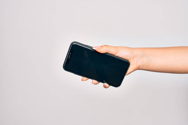 Mano de mujer joven caucásica sosteniendo teléfono inteligente que muestra la pantalla sobre fondo blanco aislado - Foto, imagen
