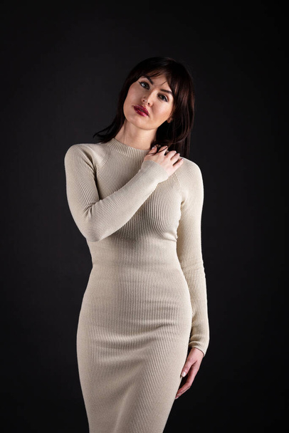 Beautiful woman in beige tight dress on black background - Фото, изображение