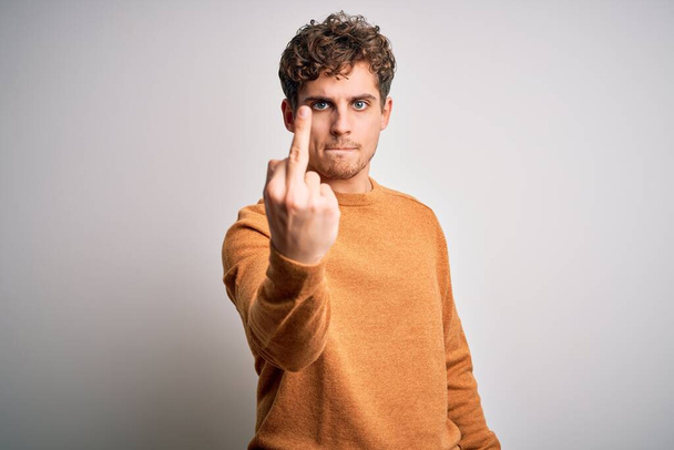 Young blond handsome man with curly hair wearing casual sweater over white background Showing middle finger, impolite and rude fuck off expression - Foto, Bild