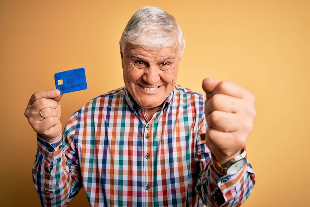 Senior handsome hoary customer man holding credit card to finance payment screaming proud and celebrating victory and success very excited, cheering emotion - Foto, afbeelding