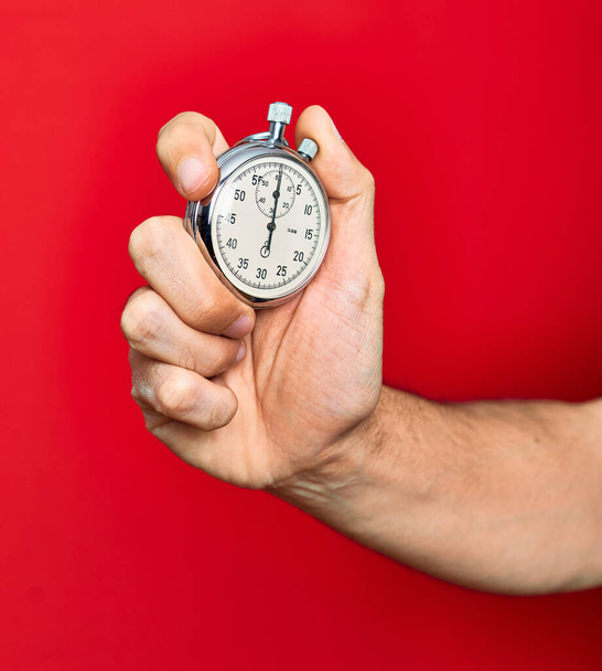 Όμορφη χέρι του ανθρώπου κρατώντας χρονόμετρο κάνει αντίστροφη μέτρηση πάνω από απομονωμένο κόκκινο φόντο - Φωτογραφία, εικόνα