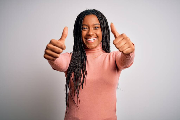 Young african american woman standing casual and cool over white isolated background approving doing positive gesture with hand, thumbs up smiling and happy for success. Winner gesture. - Photo, Image