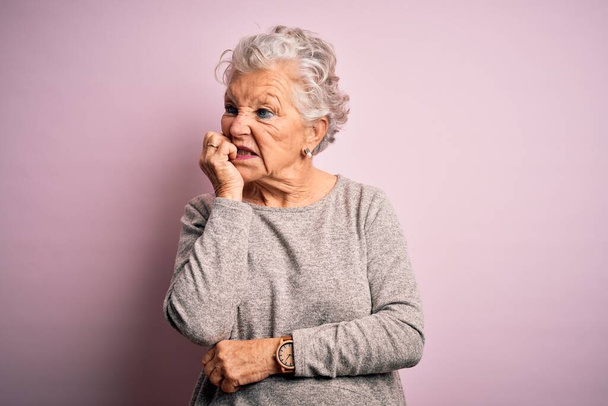 Starsza piękna kobieta w luźnej koszulce stojąca nad odizolowanym różowym tłem wyglądająca na zestresowaną i zdenerwowaną rękami obgryzającymi paznokcie. Problem lękowy. - Zdjęcie, obraz