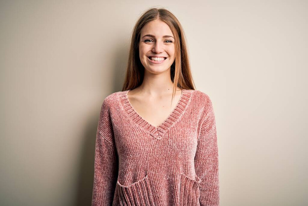 Молодая красивая рыжая женщина в розовом свитере на изолированном белом фоне с счастливой и прохладной улыбкой на лице. Счастливчик
. - Фото, изображение