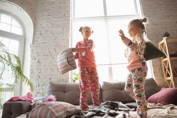 Quiet little girls playing in a bedroom in cute pajamas, home style and comfort, laughting and fighting pillows - Фото, изображение