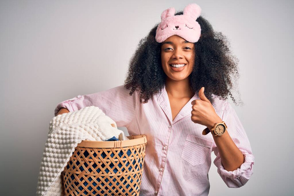 Giovane donna afro americana con i capelli afro indossando pigiama fare il bucato faccende domestiche felice con grande sorriso facendo segno ok, pollice in su con le dita, segno eccellente
 - Foto, immagini