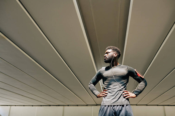 Serious muscular sportsman standing with hands on waist and looking away - Fotó, kép