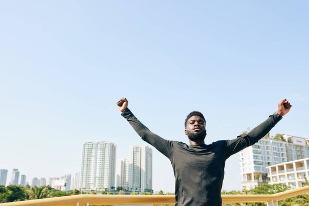 胸の開口部のための運動を行うときに腕を上げる深刻な若い黒人スポーツマン - 写真・画像