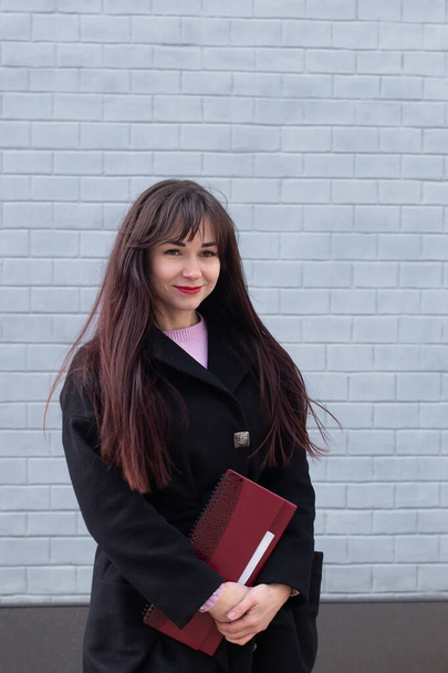 Student in black coat smiles against brick grey wall - Fotografie, Obrázek