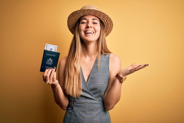 Blondynka turystka z niebieskimi oczami na wakacjach trzymając paszport Stanów Zjednoczonych z dolarami bardzo szczęśliwy i podekscytowany, zwycięski wyraz świętując zwycięstwo z wielkim uśmiechem i podniesionymi rękami - Zdjęcie, obraz