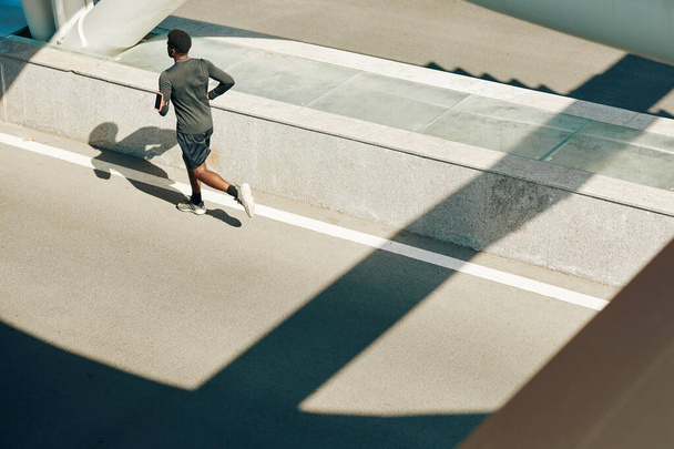 Junger schwarzer Sportler läuft in leerer Stadt auf der Straße - Foto, Bild