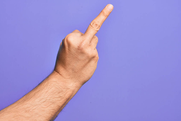 Hand of caucasian young man showing fingers over isolated purple background showing provocative and rude gesture doing fuck you symbol with middle finger - Photo, Image