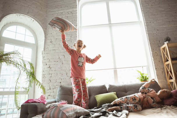 Quiet little girls playing in a bedroom in cute pajamas, home style and comfort, laughting and fighting pillows - Foto, imagen
