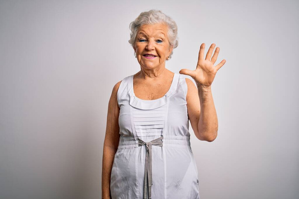 Senior beautiful grey-haired woman wearing casual summer dress over white background showing and pointing up with fingers number five while smiling confident and happy. - Photo, Image