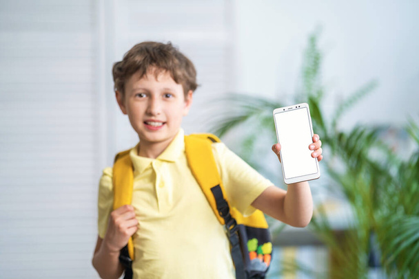 cheerful schoolboy with a backpack shows a white mobile phone screen. E-learning. Modern education with concept of mobile devices and tablets. Selective focus on the smartphone. Training platforms. - Φωτογραφία, εικόνα
