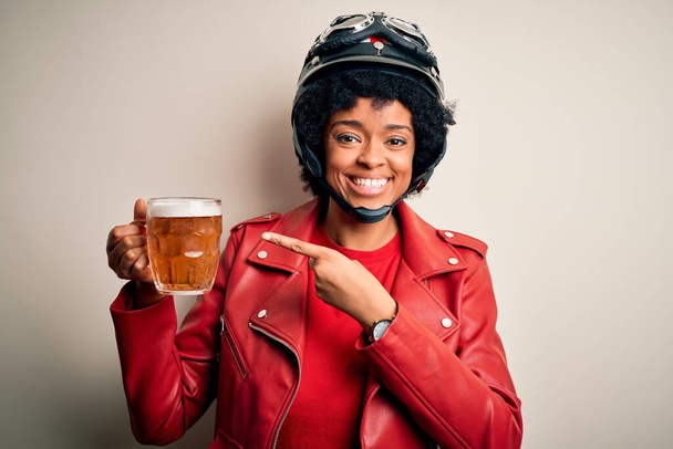 Joven afroamericana afro motociclista mujer con pelo rizado bebiendo tarro de cerveza muy feliz señalando con la mano y el dedo
 - Foto, imagen