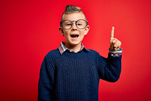 Маленький белый мальчик с голубыми глазами, стоящий в умных очках на красном фоне, указывая пальцем на успешную идею. Взволнован и счастлив. Номер один
. - Фото, изображение